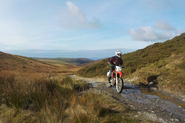 Trail rider on gravel and rock Trail rider ascending rock step with hills and sea in background